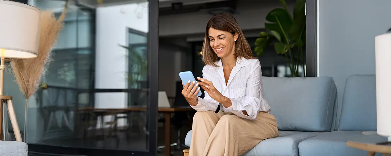 Kobieta siedząca na swoim tarasie przed domem, korzystająca z telefonu &ndash; nowoczesny dom z aluminiowymi drzwiami przesuwnymi