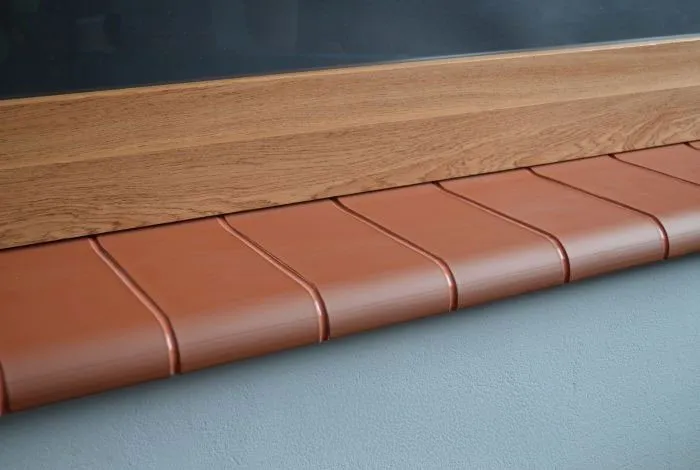 Parapet ceramiczny w kolorze czerwono-brązowym zamontowany pod drewnianym oknem na jasnej elewacji.